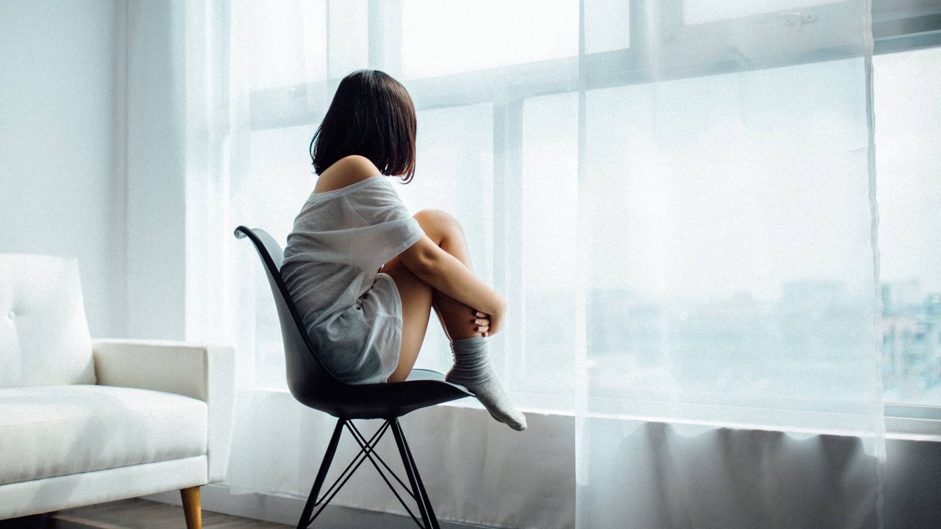 Girl sitting in front of the window and hugging her legs
